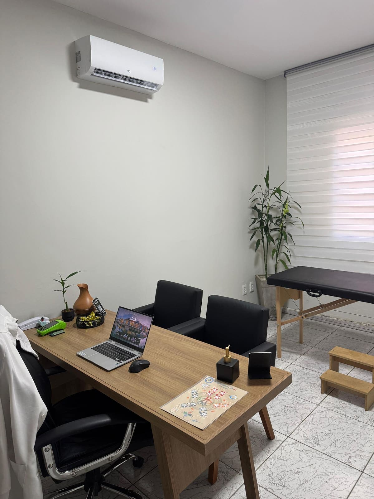 Sala de atendimento - mesa em madeira, duas poltronas em corino preto, maca em corino preto com escadinha e ar-condicionado