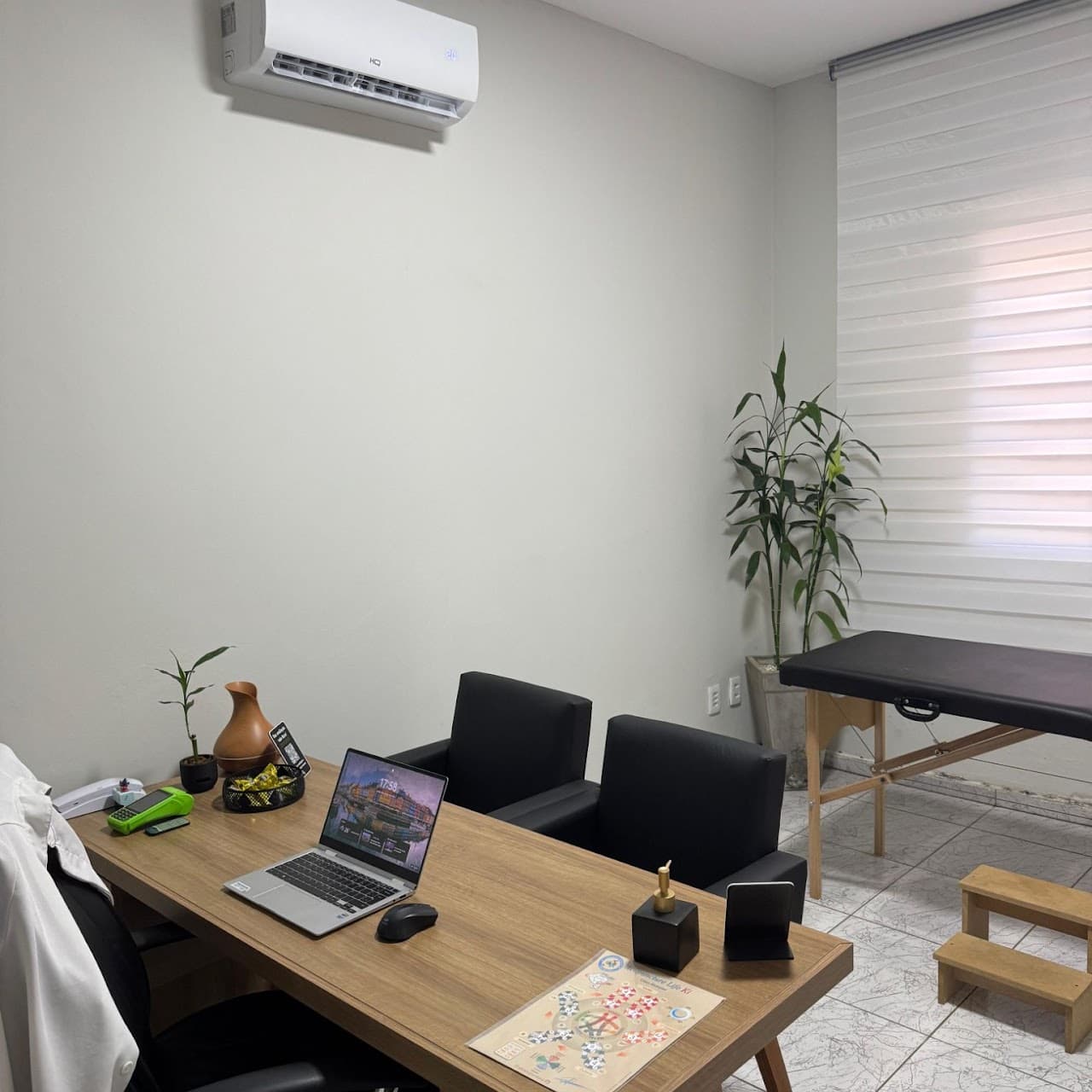 Sala de atendimento - mesa em madeira, duas poltronas em courino preto, maca em courino preto com escadinha e ar-condicionado