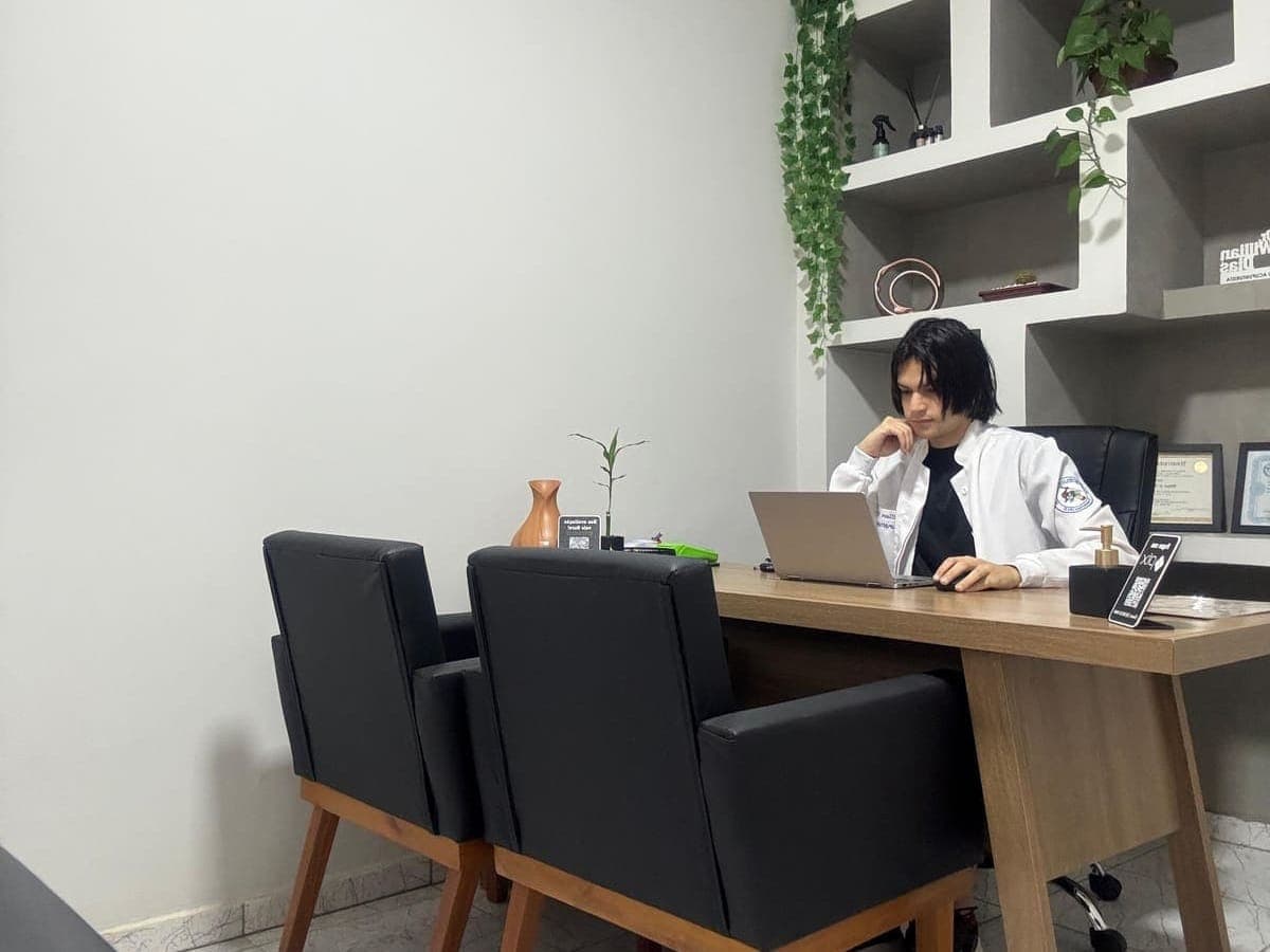 Sala de atendimento - Dr. Willian em atendimento, mesa, poltronas em courino preto e armário de nichos em alvenaria